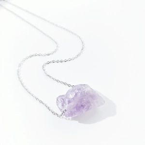 Detailed view of irregular purple natural crystal raw stone pendant on a thin silver chain