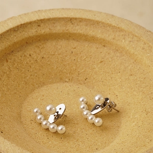 Boucles d'oreilles minimalistes en perles argentées posées sur un plat texturé