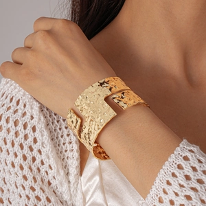 Close-up of a wide gold cuff bracelet with irregular hammered texture on a woman's wrist