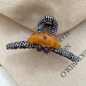 Détail de la pince à cheveux à carreaux avec breloque croissant ambrée sur fond beige