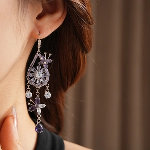 Close-up of butterfly and flower drop earrings with purple zircon crystals on ear