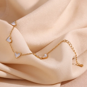 Detail of 18K gold plated bracelet with five white heart shell charms on silk background