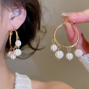 Detail of vintage gold hoop earrings with white pumpkin beads shown on ear and hand