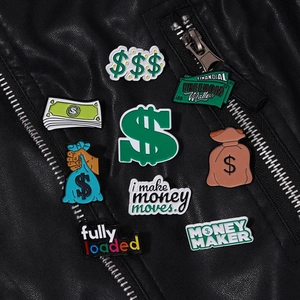 Close-up of Money Maker themed enamel pins on black leather jacket texture