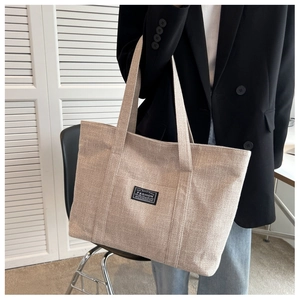 Close-up of beige canvas tote bag with fashion label shown on a model with denim jeans