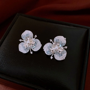 Macro shot of silver flower stud earrings with blue stones and pearls on black leather box