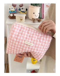 Détail d'une trousse de maquillage matelassée à carreaux rose et blanc tenue à la main