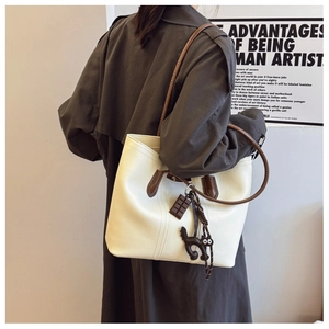 Chic beige tote bag with brown trim and cat charm shown on model's shoulder for street style