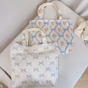 Flat lay detail of blue floral and bow canvas tote bags with simple wish label on table