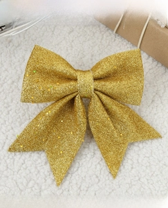Close-up of golden sequined Christmas bow decoration on white plush background