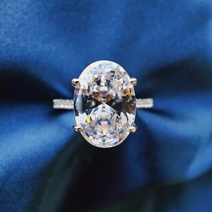 Nahaufnahme eines Rings mit ovalem Edelstein und Pavé-Besatz auf blauem Seidenstoff