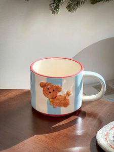 Detail of ceramic coffee mug with blue stripes and 3D brown poodle dog on a wood table