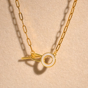 Close-up of gold chain necklace with a white circular shell inlay and OT toggle clasp