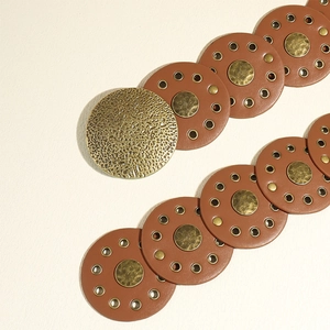 Close-up of vintage brown leather circle belt with brass rivets and hammered metal buckle
