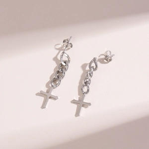 Macro detail of silver cross chain tassel earrings on a minimalist textured surface