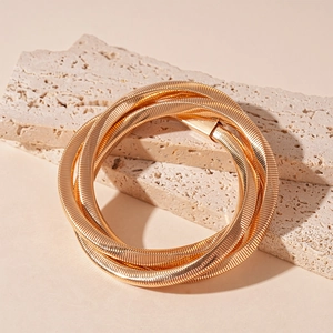 Close-up of gold multi-layer twisted snake bone bracelet on beige stone display