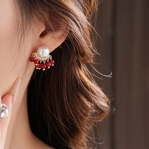 Close-up of gold tassel earrings with pearls and red beads worn on a model