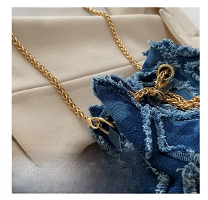 Detail of blue denim bucket bag featuring gold metal chain strap and frayed edges
