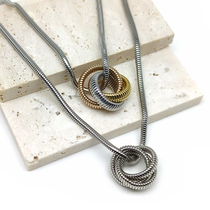 Detailed shot of interlocking three-ring pendants on flexible snake chains over beige stone