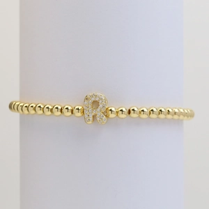 Detail of gold beaded elastic bracelet featuring a sparkling zircon micro-pave letter R charm