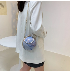 Detail of spherical acrylic evening bag with blue and white marble texture and gold chain