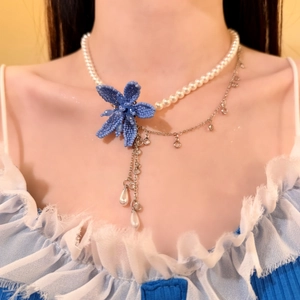 Close-up detail of a French chic necklace featuring a blue beaded flower and elegant pearls.