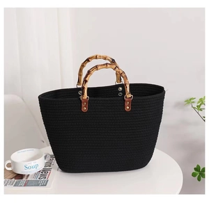Detail of hand-woven black tote bag featuring a natural bamboo handle and metal rivets