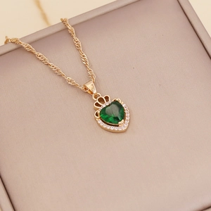 Detail of gold necklace with green heart gem pendant and crown setting on a beige box