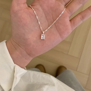 Close-up of minimalist silver necklace with rectangular clear crystal pendant in hand