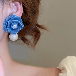 Close-up of a blue denim rose earring with pearl accents worn on a female model