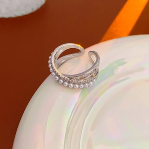 Macro shot of multilayer crisscross ring with pearls and zircon stones on white ceramic