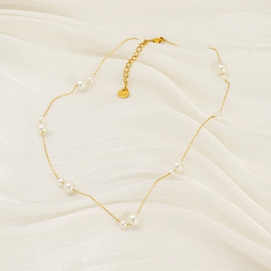 Élégant collier en titane doré avec perles blanches sur fond en soie satinée
