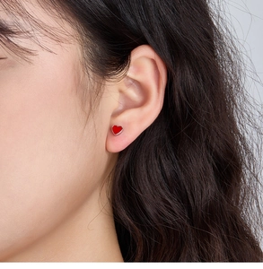 Close-up of small red heart stud earring with silver trim worn by a female model