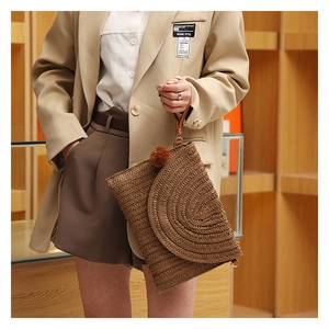 Detail of hand-woven straw clutch featuring textured flap and decorative brown pompom