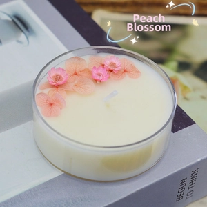 Detailed close-up of handmade soy candle with pink peach blossoms in a small glass cup