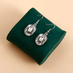 Détail de boucles d'oreilles chapeau de cowboy en argent sur un écrin en velours vert