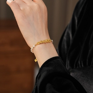 Detail of pearl bracelet with gold beads and heart charm on a vintage silk sleeve