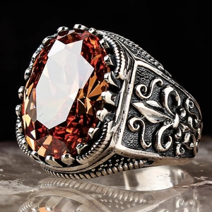 Macro shot of men's punk ring featuring a large orange oval zircon and fleur-de-lis carvings