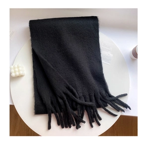 Close-up of a soft black plush scarf with tassels on a white table with a candle