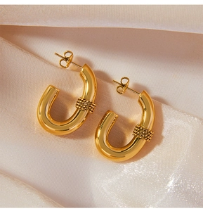Detailed shot of gold-plated U-shaped earrings with braided texture on satin fabric