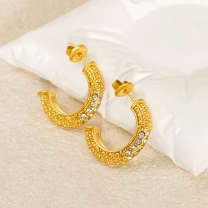 Detail of gold U-shaped earrings featuring textured surface and sparkling crystal inlays