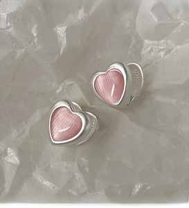Macro shot of silver heart earrings with pink cat-eye stone detail on white texture