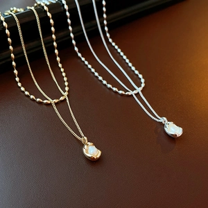 Detailed view of layered gold and silver chains featuring irregular pearl pendants