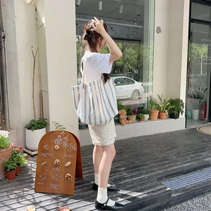 Outdoor lifestyle shot of a striped canvas tote bag with large capacity and double straps