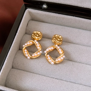 Macro detail of 18K gold plated square earrings with pearls in a velvet jewelry box