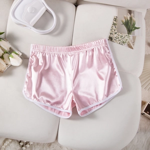 Detailed shot of pink satin yoga shorts with elastic waist and white trim on sofa