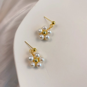 Elegant gold flower stud earrings with natural freshwater pearls on a clean cream background