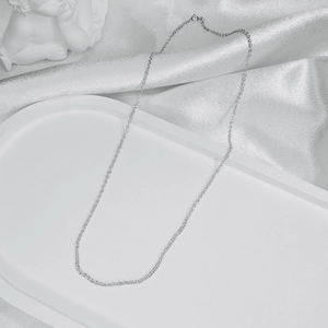 Close-up of minimalist silver chain necklace on white satin with an angel statue