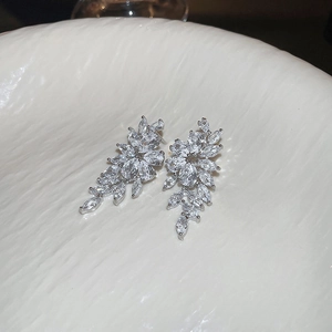 Close-up of zircon leaf tassel earrings on a textured white ceramic display plate