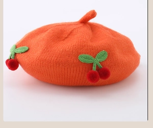 Close-up of cute knitted cherry appliques on a bright orange baby wool beret hat